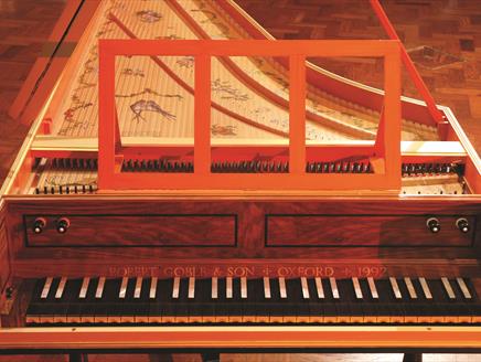 An old harpsichord made of wood, with etchings of birds and flowers on the top. Above the keys, etched are the words 'Robert Goble & Son / Oxford / 19