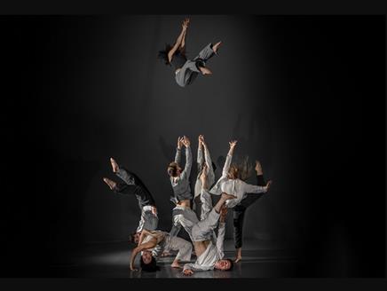 A group of dancers dressed in grey clothes one of the dancers has been thrown up.