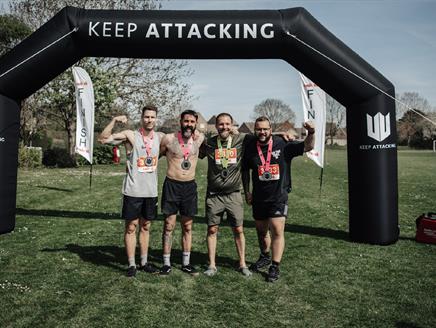 Four men with medals stood in front of an inflatable arch saying Keep Attacking.