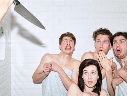 Three men, one woman in towels in a shower someone is holding a knife up out of shot and they look shocked.