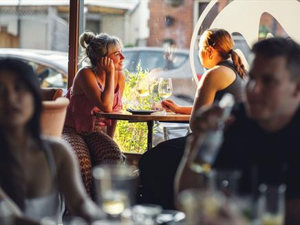 customers enjoying conversation over a glass of wine with dappled sunlight through the window