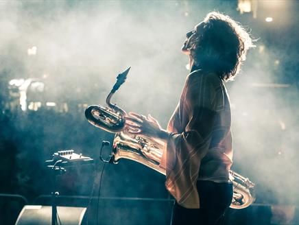 Tamar Osborn is facing away, holding her baritone saxophone with smoke in the background