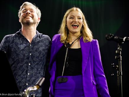 Emma Rawicz and Gwilym Simcock stand side by side smiling next to a microphone.