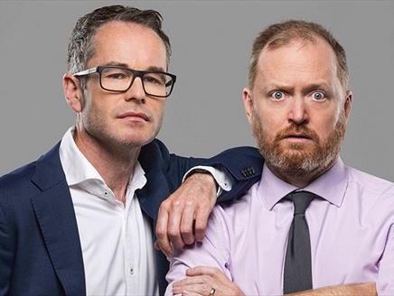 Two white men, one wearing glasses with a shirt and jacket. The other has a beard with a shirt and tie.