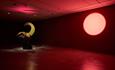 Image of artist Jala Wahid's work Conflagration, showing a sculptural work in the middle of a red lit gallery space, with a pink circle on the wall.
