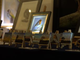 small canvases set up on a table, depicting sunny skies and robins