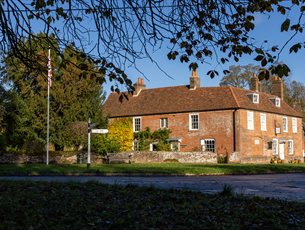 Jane Austen's House from the garden in Autumn.  Brown and orange leaves carpet the ground. 