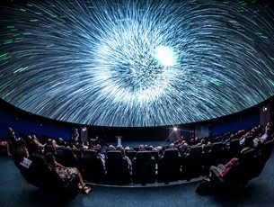 A blast of white light on a Planetarium dome. There are people sat in seats watching the screen.