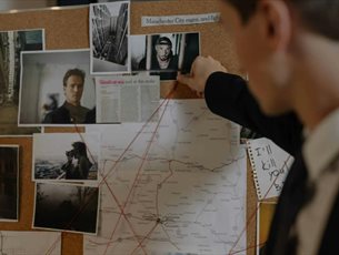Person examining a map on a bulletin board with various images and notes.