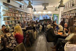 Groups of people sitting at tables in a bookshop with drinks taking part in a quiz