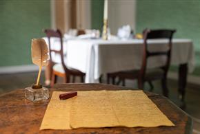 Jane Austen's small wooden writing table. A quill and letter sit on the table.