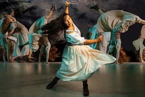 A woman in a white dress dances energetically, captured in mid-motion with multiple blurred images of her spinning in the background.