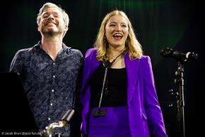 Emma Rawicz and Gwilym Simcock stand side by side smiling next to a microphone.