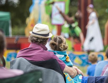 focus on backs of outdoor audience with performance blurred in the background