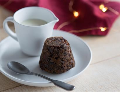 Christmas pudding on a white plate next to a jug of cream.