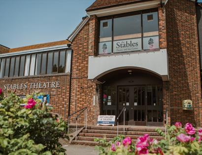 Exterior of The Stables Theatre, Hastings, a brick-built arts venue framed by colourful flower beds.