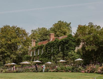 Pashley Manor house framed by flower-filled borders, lawns and mature trees in the gardens.