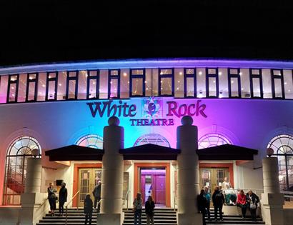 White Rock Theatre exterior lit at night with colourful lights and visitors gathered outside entrance.
