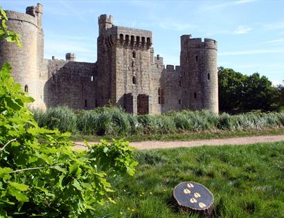 photograph of turreted castle with grass lawn in foreground, includes a small plaque on grass with painted hoofprints