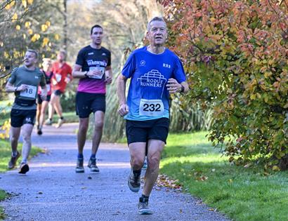 Runners take part in the Bedgebury Forest 10 & 5 Mile race along a tree-lined path surrounded by autumn colours