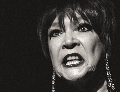 a black and white photograph, close up portrait of a woman's face with completely black background. Woman has dark lipstick and bears her teeth in an