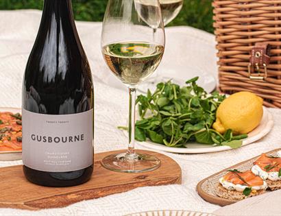 close up shot of picnic blanket laid with gusbourne wine, salmon canapes and rocket and lemon, hamper in background