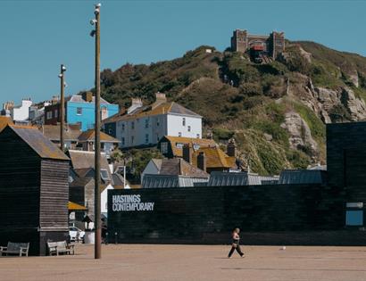 Hastings Contemporary gallery beneath East Hill cliffs, with Old Town buildings and fishing huts nearby.