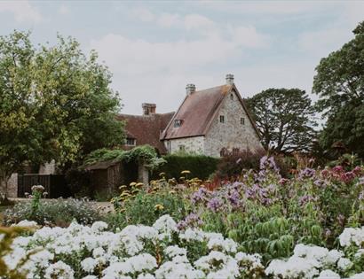 Michelham Priory surrounded by colourful flower beds and mature trees in the historic gardens.