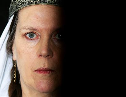 close up portrait of a white woman staring coldly at the camera, one half of face in complete shadow, a crown slightly visible