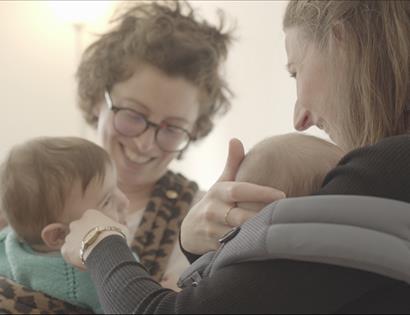 VoxSling event at The Crown Hastings: adults with babies sharing a warm, close moment in a softly lit indoor setting.