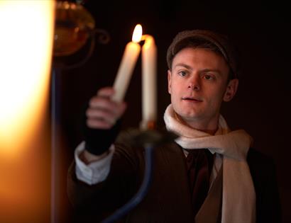 a young man wearing a cap and scarf lighting a candle.