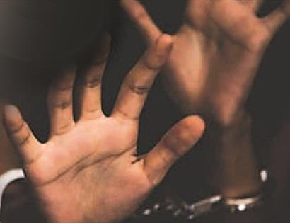 a photograph of a black person's hands reaching towards the camera with a blurred background. Handcuffs just visible.