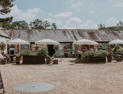 Michelham Priory courtyard café with outdoor seating, historic buildings and flower-filled planters.