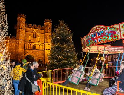 Nightime scene of children's carousel with Battle Abbey illuminated in the background.