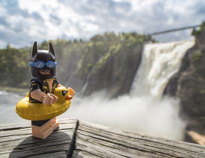 lego batman figure wearing rubber ring on a ledge with a waterfall in the background.
