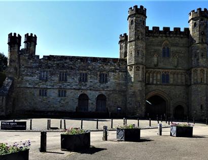 a landscape photograph of the entrance to Battle Abbey. A long brick building with turrets and crenellated walls.