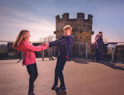photograph of two children holding both hands on viewing platform with turret.