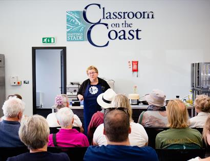 a photograph of a cookery classroom with a teacher, CJ Jackson, in the front, rows of backs of heads.