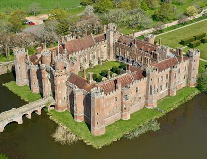 Aerial view of Herstmonceux Castle surrounded by a moat, gardens, and green parkland.