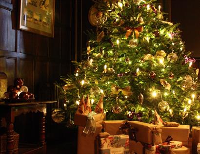traditional christmas tree aglow with warm lights and brown parcels beneath.