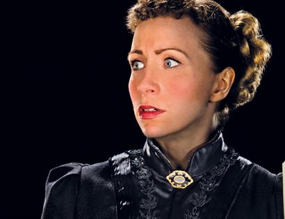 A photograph of a woman with a shocked expression holding a torch in the darkness