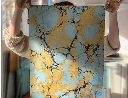 A person holds a large piece of marbled paper in front of their face.