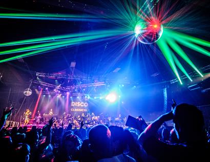 photo showing crowded club night with green lasers and disco ball,