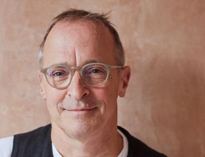 A close up of a white man smiling, wearing plastic rimmed glasses.