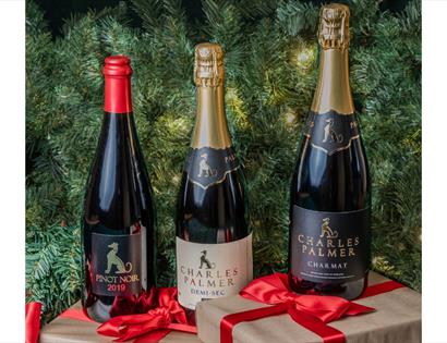 Three Charles Palmer wine bottles with festive ribbons in front of a green Christmas tree background.