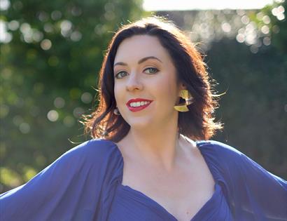 Headshot photograph of a woman smiling with red lipstick, she wears a blue dress