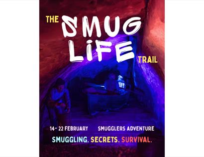 Poster for ‘The Smug Life Trail’ with figures in a cave lit in red and blue, promoting a smuggling‑themed event.