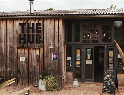Exterior of The Hub at Quarry Farm near Bodiam, with wooden cladding, entrance doors, signs and an outdoor seating area.