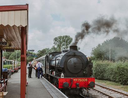 Kent and East Sussex Heritage Railway with a black steam locomotive at a station platform, emitting smoke.