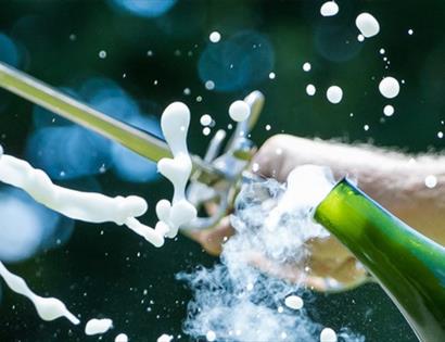 A sword slices open a champagne bottle, sending spray and foam bursting into the air.